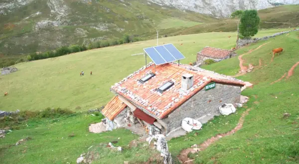 Refugio en Picos de Europa, con paneles solares en el tejado. Vacas pastan en la ladera verde.