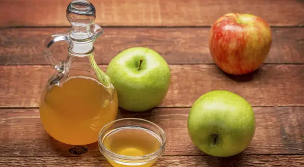 Apfelessig in einer Karaffe und Schale, daneben Äpfel. Vielseitige Apfelessig Anwendung für Küche und Gesundheit.
