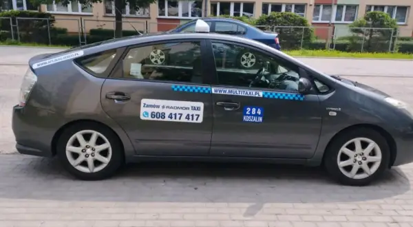 Szary hybrydowy Prius z napisem "284 KOSZALIN" i numerem telefonu do zamówienia taksówki.