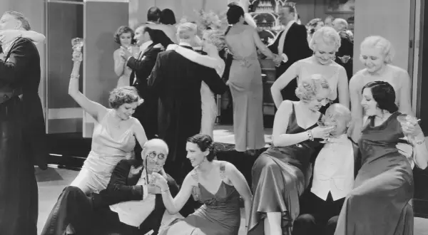 Zabawa towarzyska w stylu dwudziestolecie międzywojenne ramy czasowe. Eleganckie kobiety i mężczyźni w strojach z epoki, toastowanie i tańce.