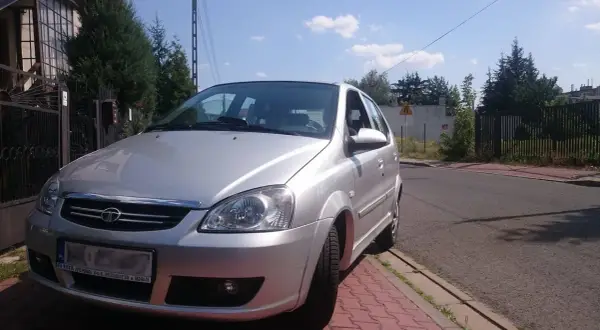 Srebrny tata indica zaparkowany przy czerwonym chodniku. W tle dom i drzewa.