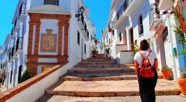 Una mujer con mochila sube escaleras empedradas en un pintoresco pueblo blanco, quizás el pueblo mas bonito de Andalucia.