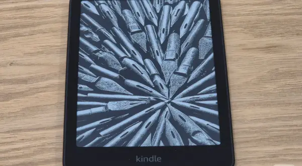 Un Kindle, une liseuse électronique affichant une image abstraite de plumes d'encre, sur un fond en bois.