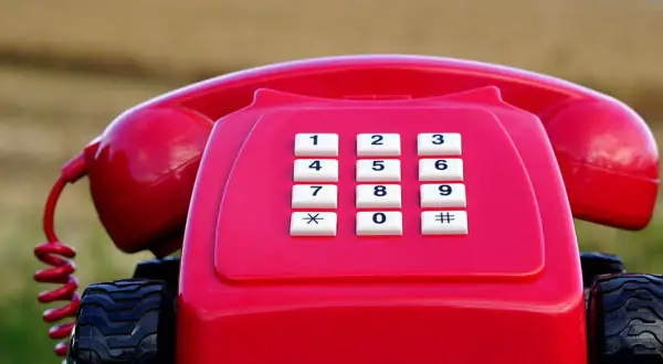 Czerwony telefon stacjonarny na kółkach, jakby gotowy do podróży po najtańszy abonament.