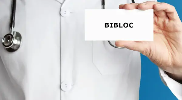 Lekarz w białym kitlu trzyma wizytówkę z napisem BIBLOC. Stetoskop wisi na jego szyi.