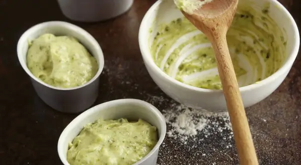 Kleine Förmchen werden mit einer grünen Masse gefüllt, die nach Pistaziencreme selber machen aussieht. Ein Holzlöffel liegt in einer Schüssel mit der Masse.