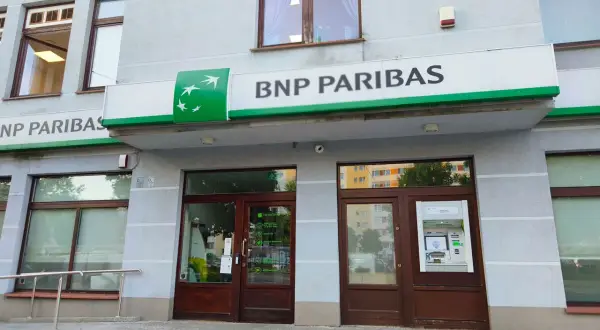 Wejście do placówki banku BNP Paribas z zielonym logo i napisem. Obok drzwi znajduje się bankomat.