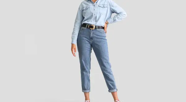 Modelka w jasnych jeansach z podwiniętymi nogawkami i jeansowej koszuli. Idealne jeansy dla niskiej osoby, które optycznie wydłużają nogi.