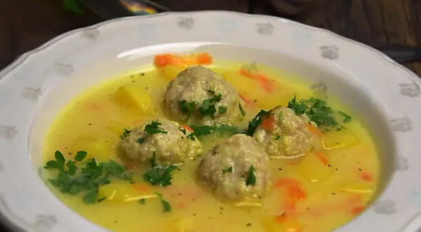 Zupa klopsowa babci: pyszne klopsiki w żółtym, kremowym sosie z ziemniakami i marchewką, posypana natką pietruszki.