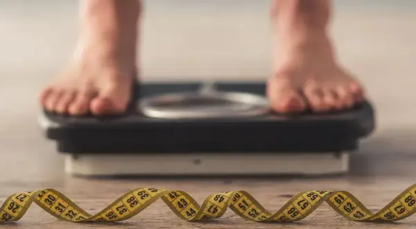 Pieds sur une balance, ruban à mesurer enroulé au premier plan. La question "pourquoi je ne perds pas de poids" résonne.