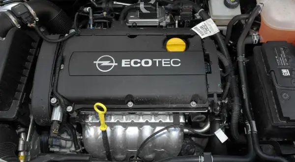 Silnik Ecotec w samochodzie Opel Astra H. Widoczny jest czarny dekiel z logo Opla i napisem Ecotec, żółta miarka oleju oraz elementy układu chłodzenia i dolotowego.