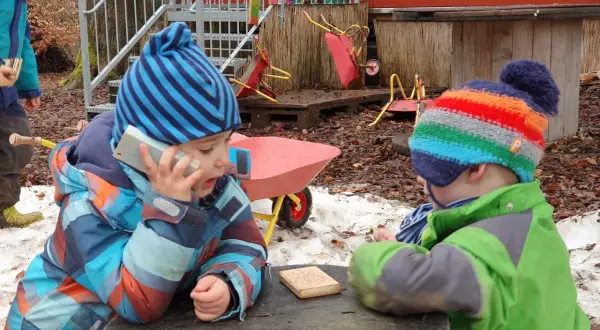 Zwei Kinder im Wald Kindergarten spielen mit einem Spielzeugtelefon und einem Holzklotz.
