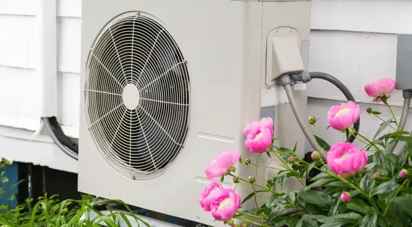 Unità esterna di una pompa di calore ad aria, con fiori rosa in primo piano.