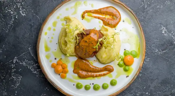 Talerz z pieczoną wieprzowiną, puree ziemniaczanym i sosami.