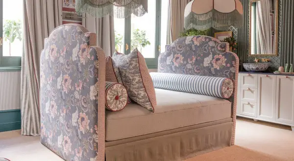 Un cabecero tapizado con flores rosas y azules, bordes a rayas y cojines a juego. Inspiración para como tapizar un cabecero.