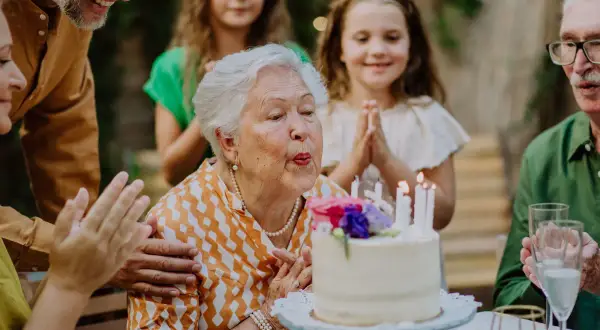 Babcia zdmuchuje świeczki na torcie, rodzina składa życzenia na 51 urodziny.