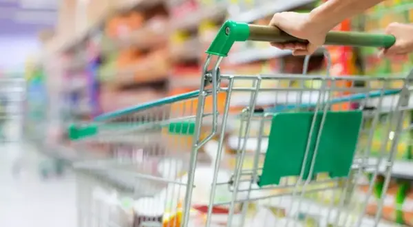 Ręka pcha wózek sklepowy w alejkach sklepu spożywczego, tworząc obraz dynamicznego doświadczenia w branży retail.
