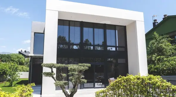 Moderna casa con fachada gris y beige, grandes ventanales y jardín cuidado.