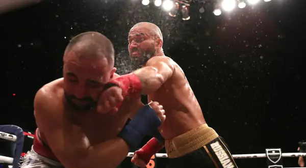 En slagväxling i MMA-ringen. En fighter med röd lindning på handen levererar en kraftfull träff mot motståndarens ansikte. Kanske är detta den bästa MMA-fightern i aktion.