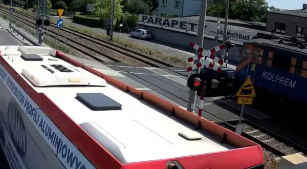 Autobus czeka na przejazd kolejowy w drodze do Częstochowy. Pociąg Kolprem mija przejazd.