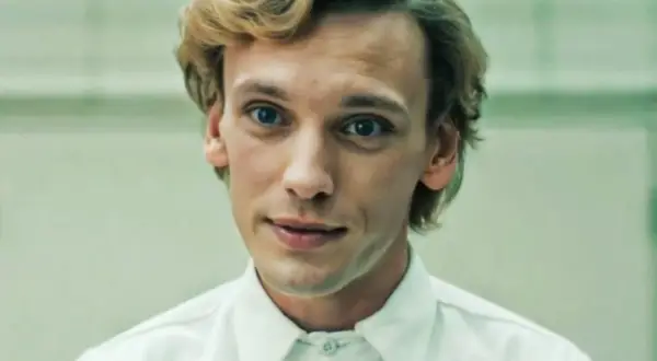 Jamie Campbell Bower, aktor wcielający się w postać Vecny, z niebieskimi oczami i blond włosami, w białej koszuli.
