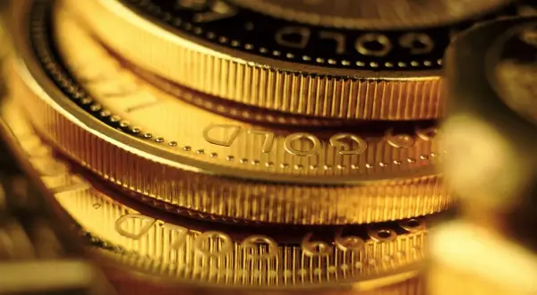 Zbliżenie na stos złotych monet z widocznym napisem "GOLD".
