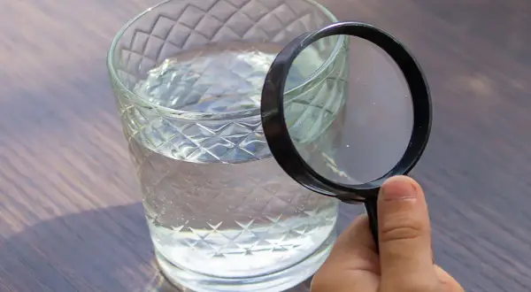 Une main tient une loupe pour analyser l'eau d'un puits dans un verre.
