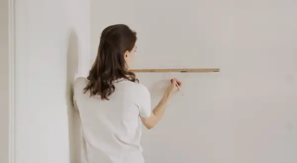 Frau misst die Wand, um zu entscheiden, wo anfangen mit dem Tapezieren.