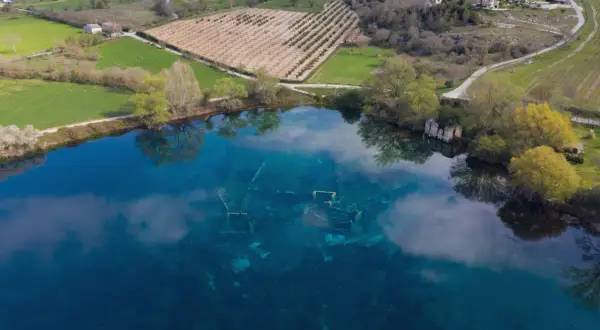 Le rovine sommerse nel lago azzurro evocano un'Atlantide d'Abruzzo. Campi verdi e alberi circondano questo luogo magico.