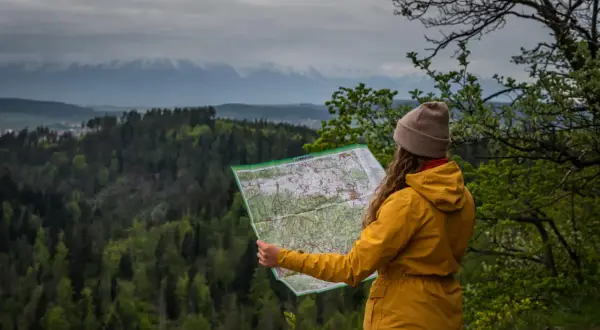 Kobieta w żółtej kurtce planuje, co zwiedzić na Słowacji, studiując mapę na tle górskiego krajobrazu.