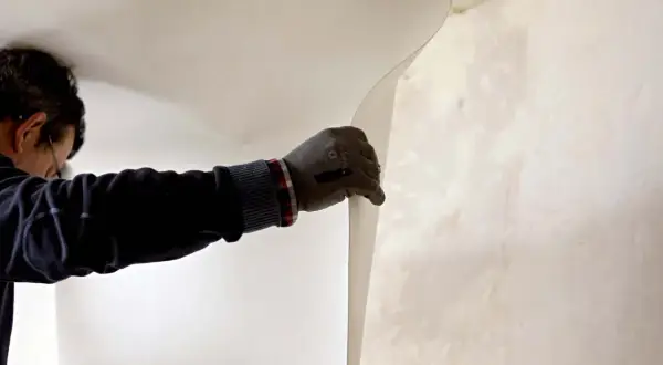 Un ouvrier pose de la fibre de verre dans les angles d'un mur.