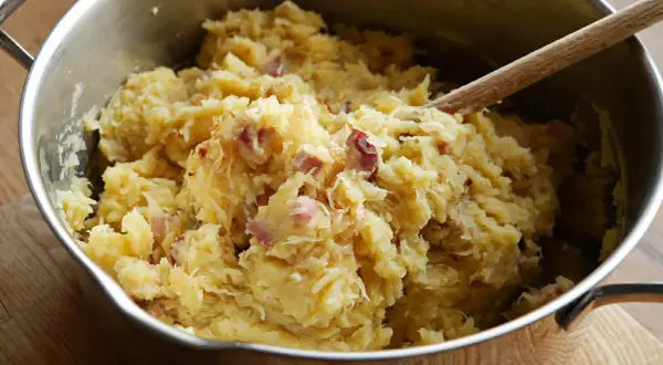 Panczkraut w garnku, gotowy do podania. Drewniana łyżka miesza ziemniaczaną masę z kawałkami boczku.