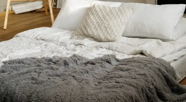 Szara, puszysta narzuta na łóżko 160x200, idealna do przytulnego wnętrza. Biała pościel i ozdobna poduszka dodają elegancji.