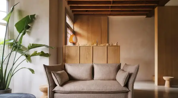 Gemütliches Wohnzimmer mit beigem Sofa, großer Zimmerpflanze und einem Schrank aus hellem Holz, der zum holz streichen einlädt.