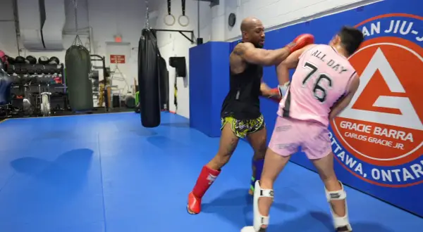 Two fighters practice boxing head movement drills in a gym. One throws a punch while the other dodges.