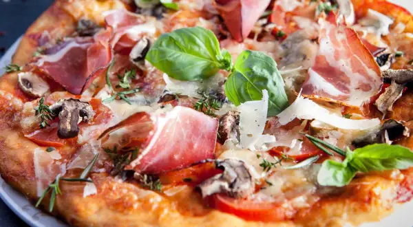Pyszna pizza parma z szynką, pieczarkami, pomidorami i bazylią, posypana parmezanem.