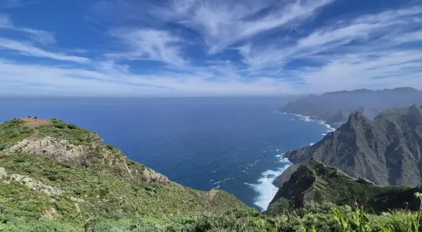 Vista del Roque de Tábarno, un promontorio verde y rocoso que se adentra en el mar azul bajo un cielo nublado.