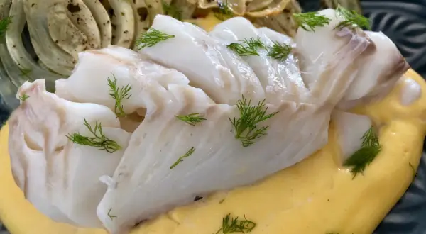 Vit fisk serveras med krämig sås och ugnsbakad fänkål, garnerad med dill.