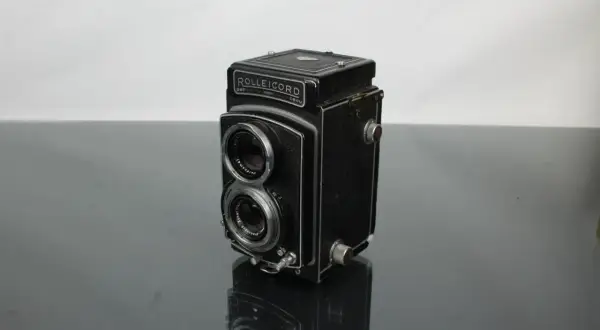 A vintage Rolleicord camera sits on a reflective surface, its twin lenses and classic design hinting at a rich photographic history.
