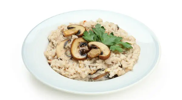 Kremowy ryż do risotto z pieczarkami i natką pietruszki na jasnoniebieskim talerzu.