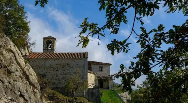 L'eremo di Cerbaiolo, con la sua torre campanaria in pietra, si staglia contro un cielo azzurro tra i rami di una quercia.