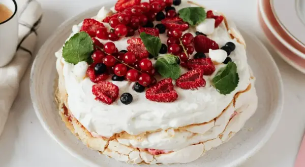 Pavlova z kremem do bezy, ozdobiona świeżymi malinami, borówkami i porzeczkami.