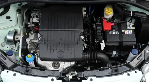Silnik w fiat 500 l. Widoczny akumulator, osłona silnika z logo FIAT, zbiorniczki płynów i elementy układu dolotowego.