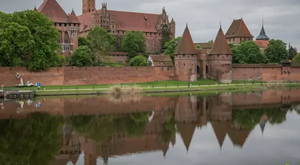 Potężny zamek w Malborku odbija się w wodzie. Sprawdź zamek w Malborku cennik i zaplanuj wizytę w tym historycznym miejscu.