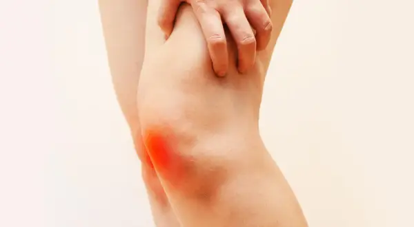 Mano che preme sul ginocchio con un'area rossa che indica dolore al ginocchio a letto.