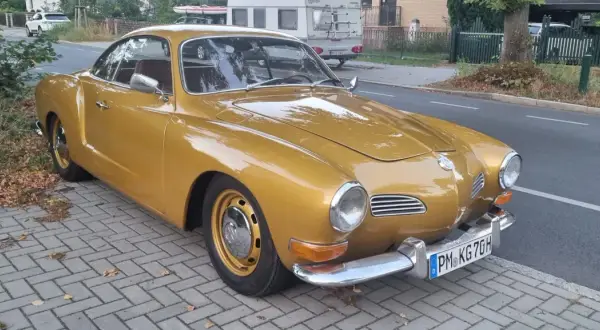 Złoty Karmann Ghia, klasyk z lat 60., lśni na tle ulicy.