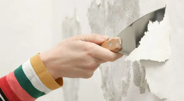 Mano con spatola che rimuove vernice a smalto scrostata dal muro.
