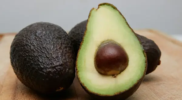 Dwa całe awokado i jedno przekrojone na pół, z widocznym pestką. Idealne do zdrowej diety, choć awokado kcal warto znać.