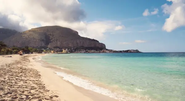 Piękna plaża Mondello z turkusową wodą, piaszczystym brzegiem i malowniczym miasteczkiem u podnóża góry.