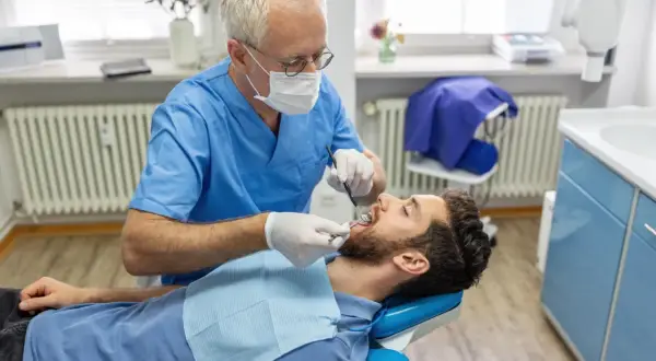 Dentysta bada pacjenta. Zastanawiasz się, ile kosztuje usunięcie ósemki na NFZ? Wizyta u stomatologa to pierwszy krok.